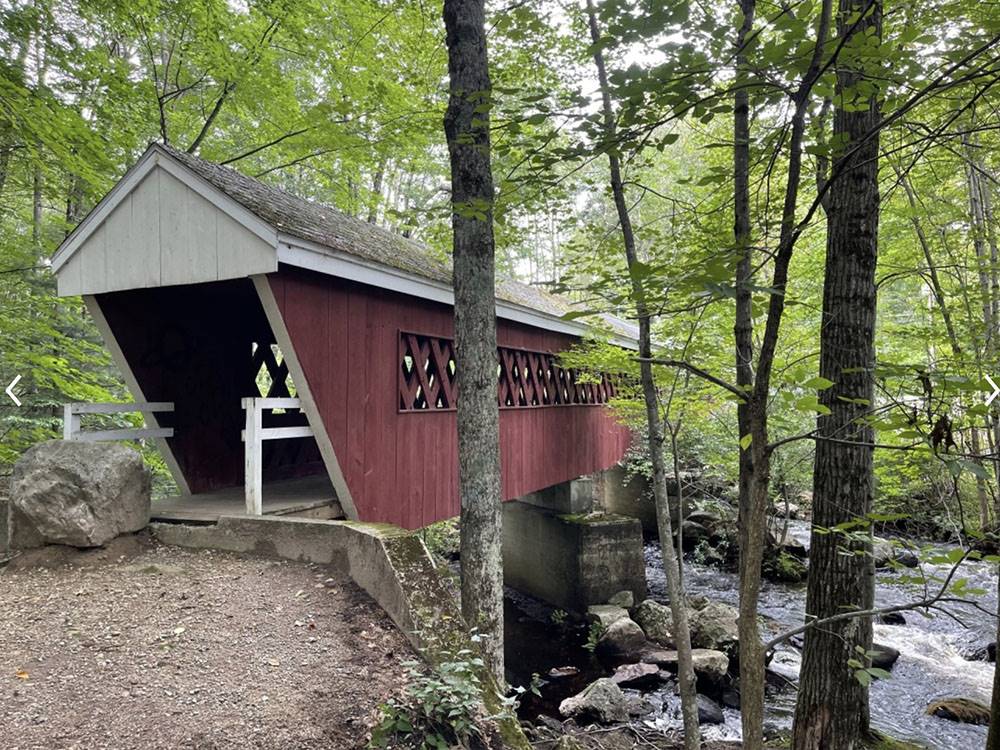 A red covered bridge over the stream at FIELD & STREAM RV PARK