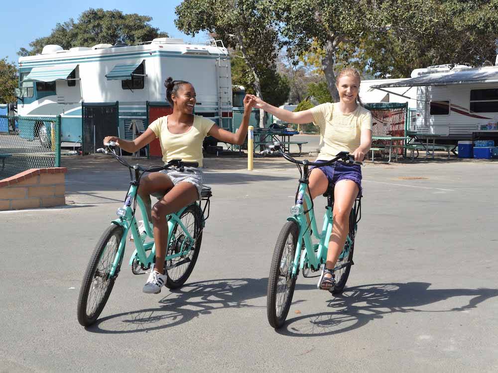 A couple of girls holding hands riding bikes at CAMPLAND ON THE BAY