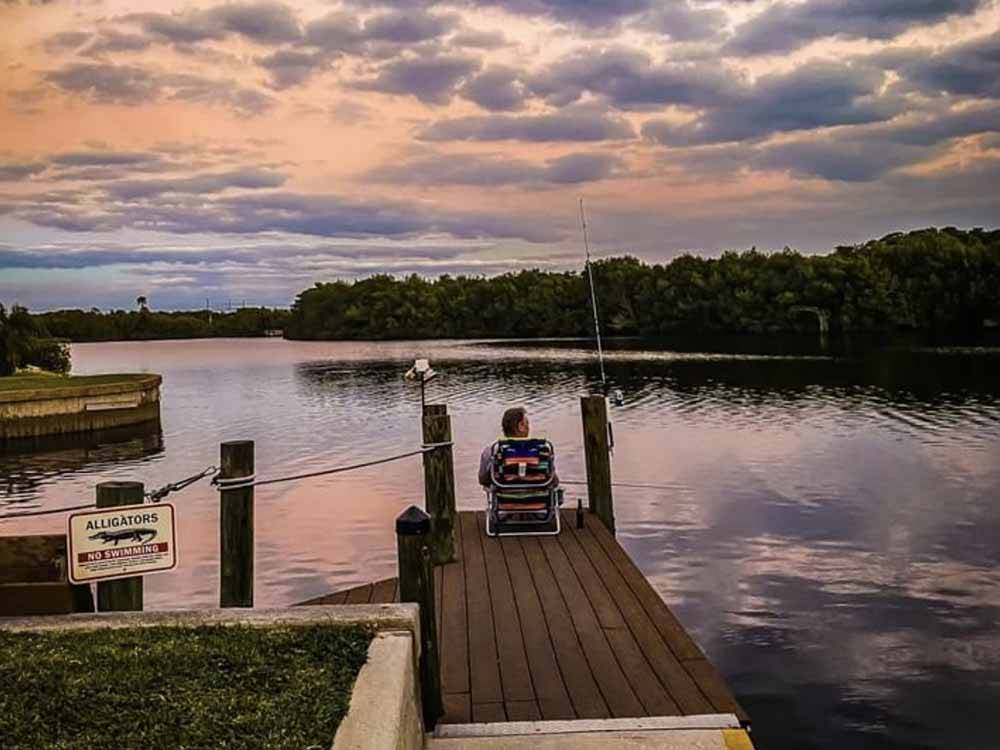 A man sitting in a chair on the pier fishing at UPRIVER RV RESORT