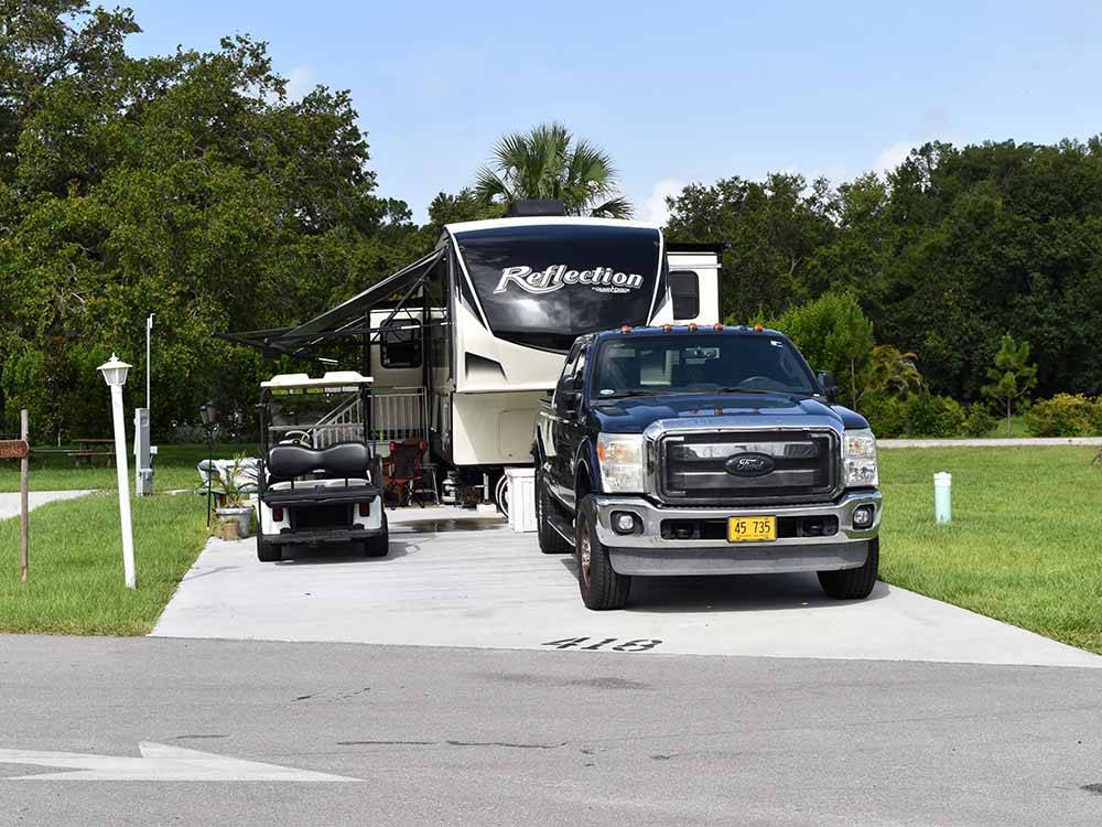 A fifth wheel trailer, truck and golf cart in a paved RV site at UPRIVER RV RESORT