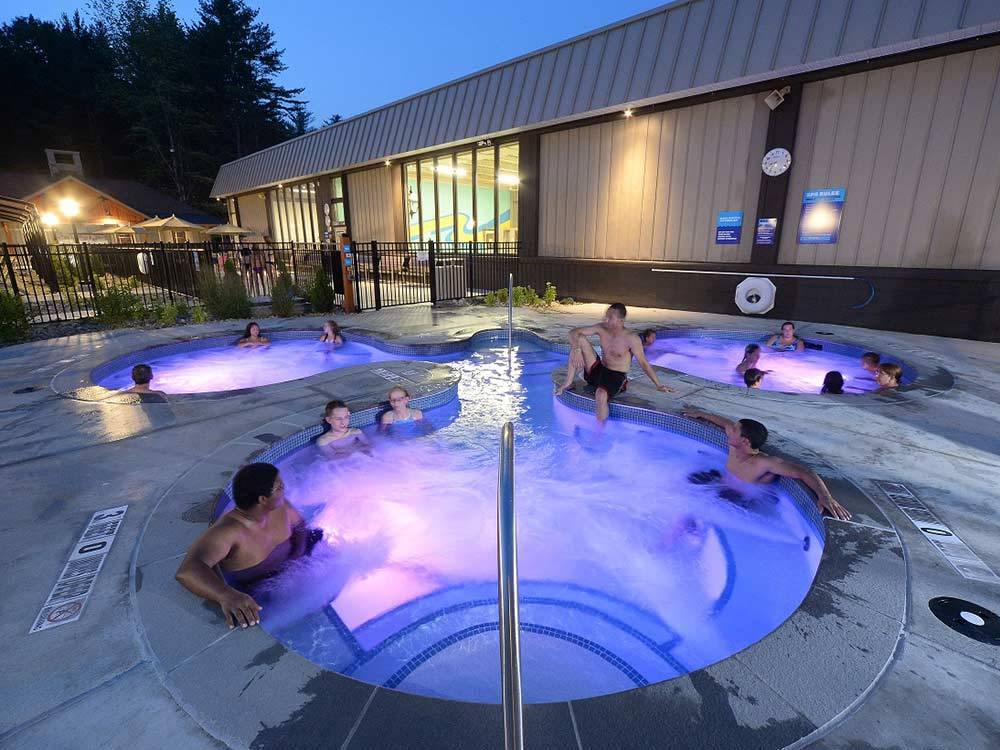Outdoor hot tub lit in purple hues at night with several people relaxing in it at LAKE GEORGE RV PARK