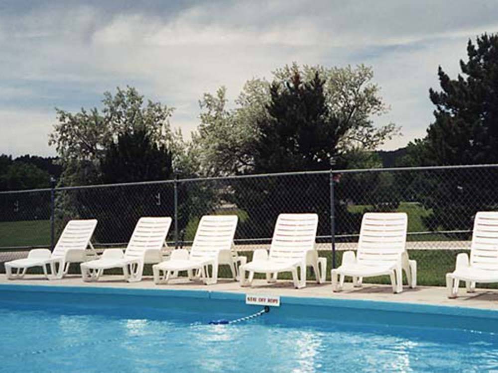 White lounge chairs next to the pool at HAPPY HOLIDAY RV RESORT
