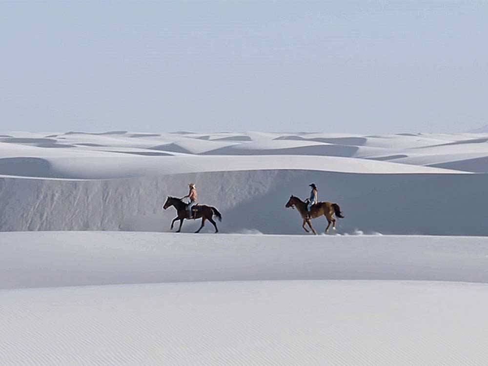 Two people riding horses on a white dune at WHITE SANDS MANUFACTURED HOME AND RV COMMUNITY
