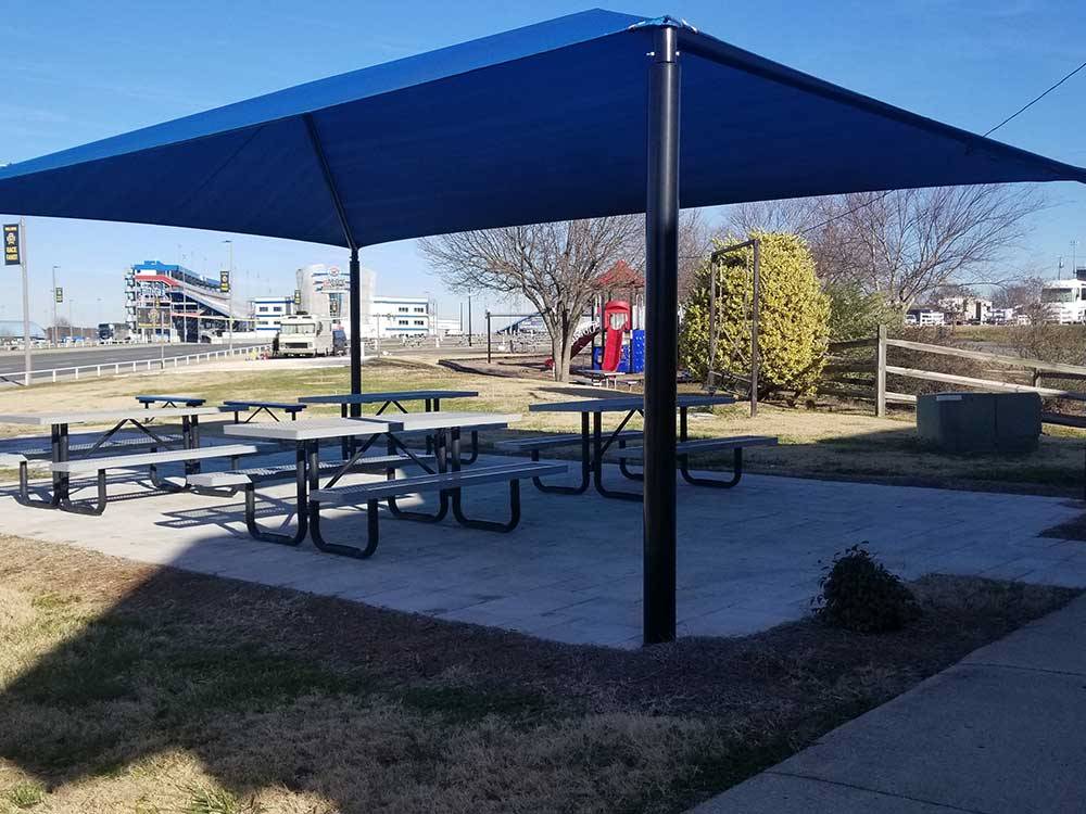 Picnic patio area under blue cover with playground in background at CAMPING WORLD RACING RESORT