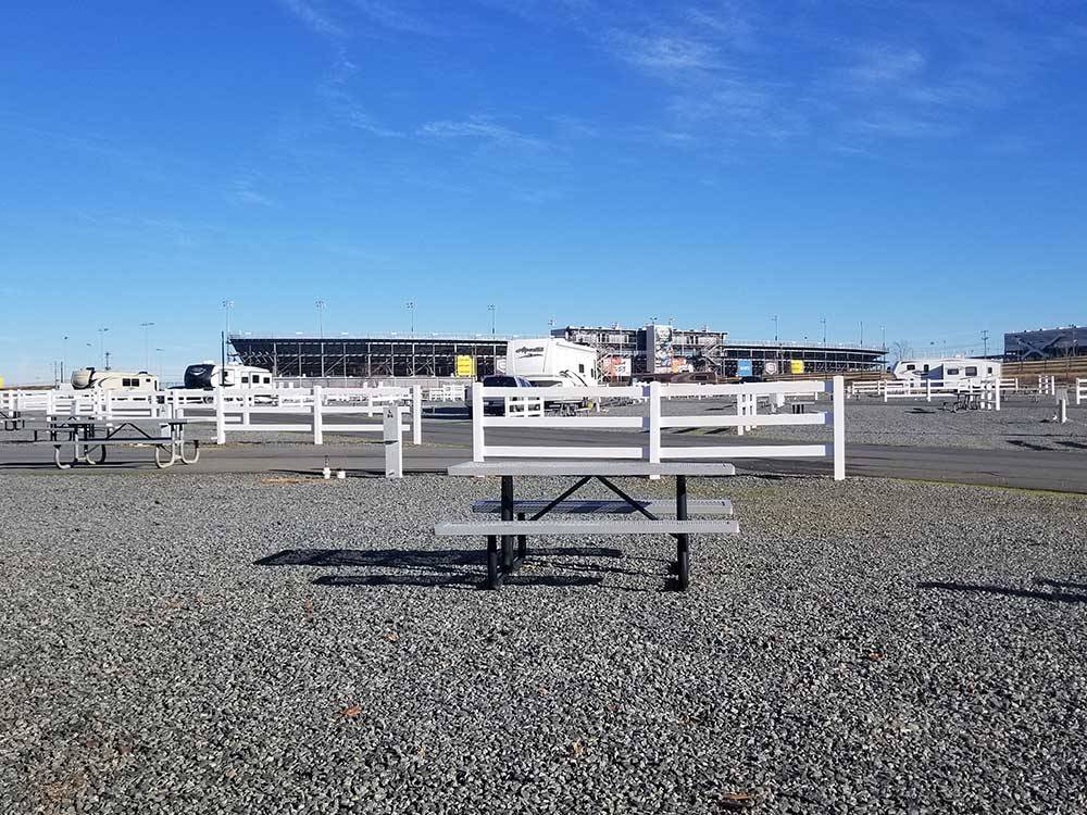 Picnic table on gravel with white fencing and large raceway in background at CAMPING WORLD RACING RESORT