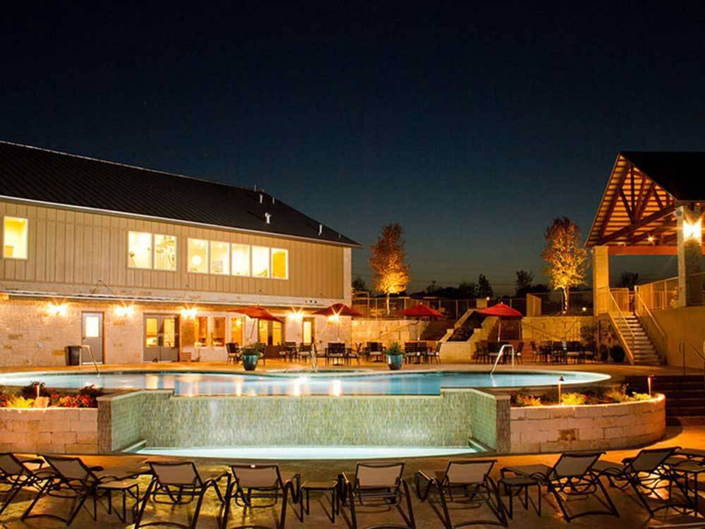 Pool with waterfall surrounded by resort buildings at night at ALSATIAN RV RESORT & GOLF CLUB