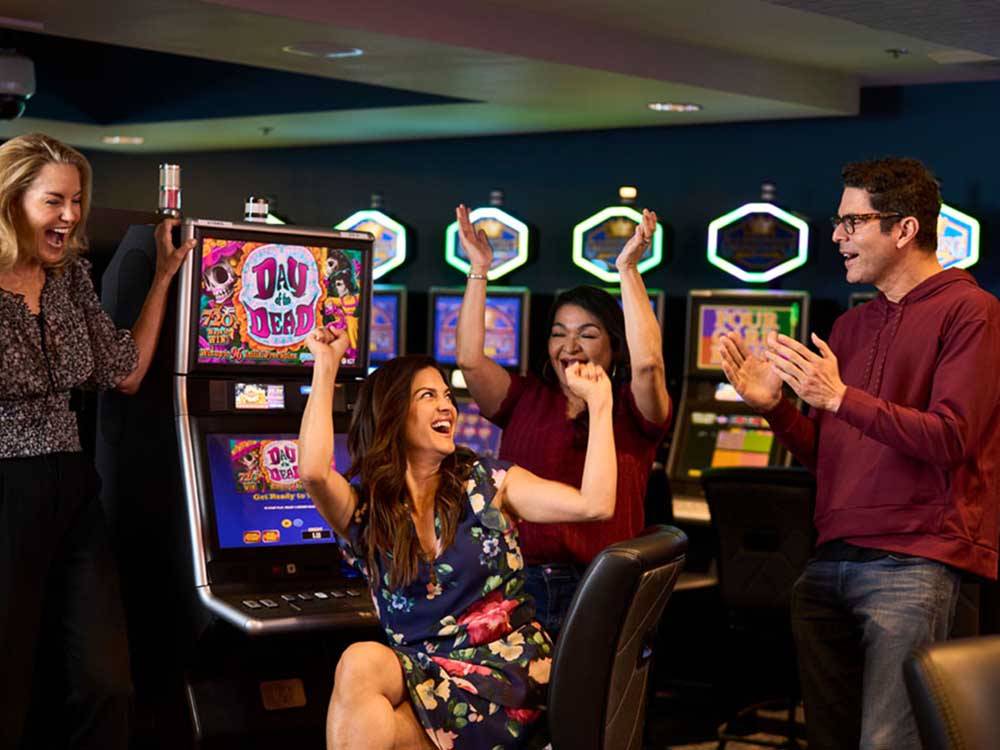 A group of people cheering at a slot machine at THE RV PARK AT ROLLING HILLS CASINO AND RESORT