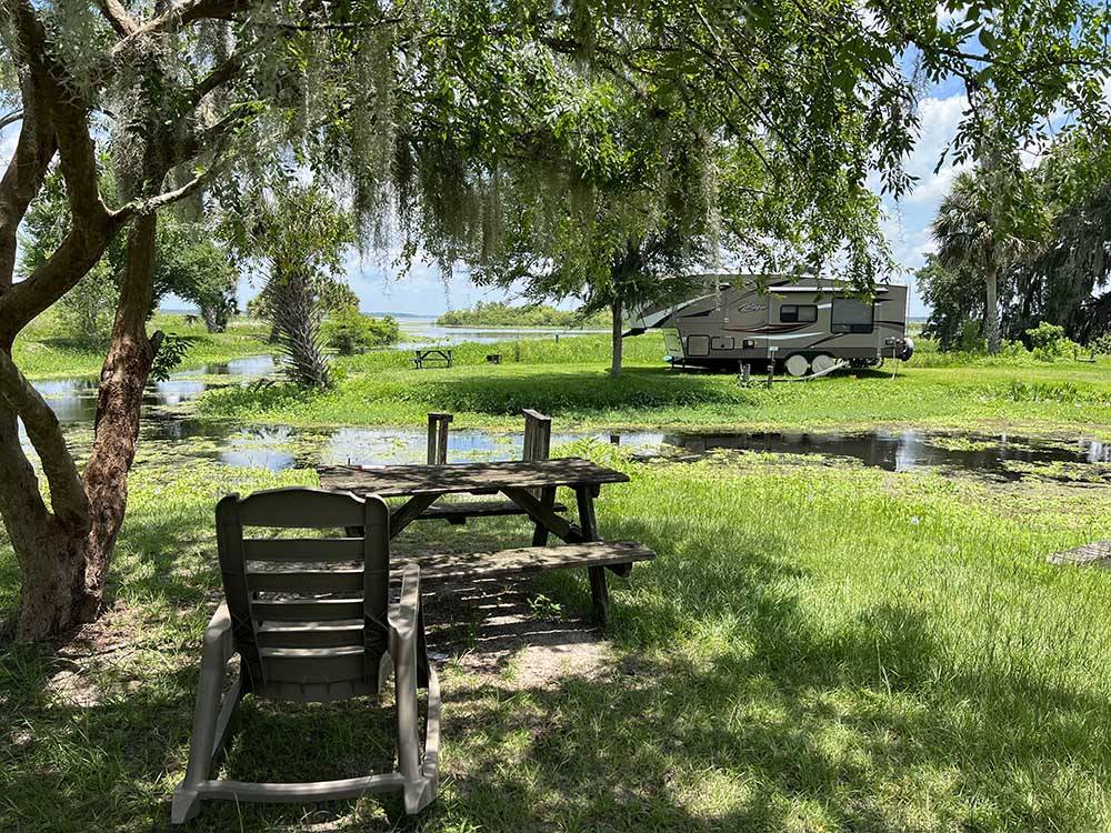 A chair and bench under a tree with a trailer in the distance at SPORTSMAN'S COVE RESORT