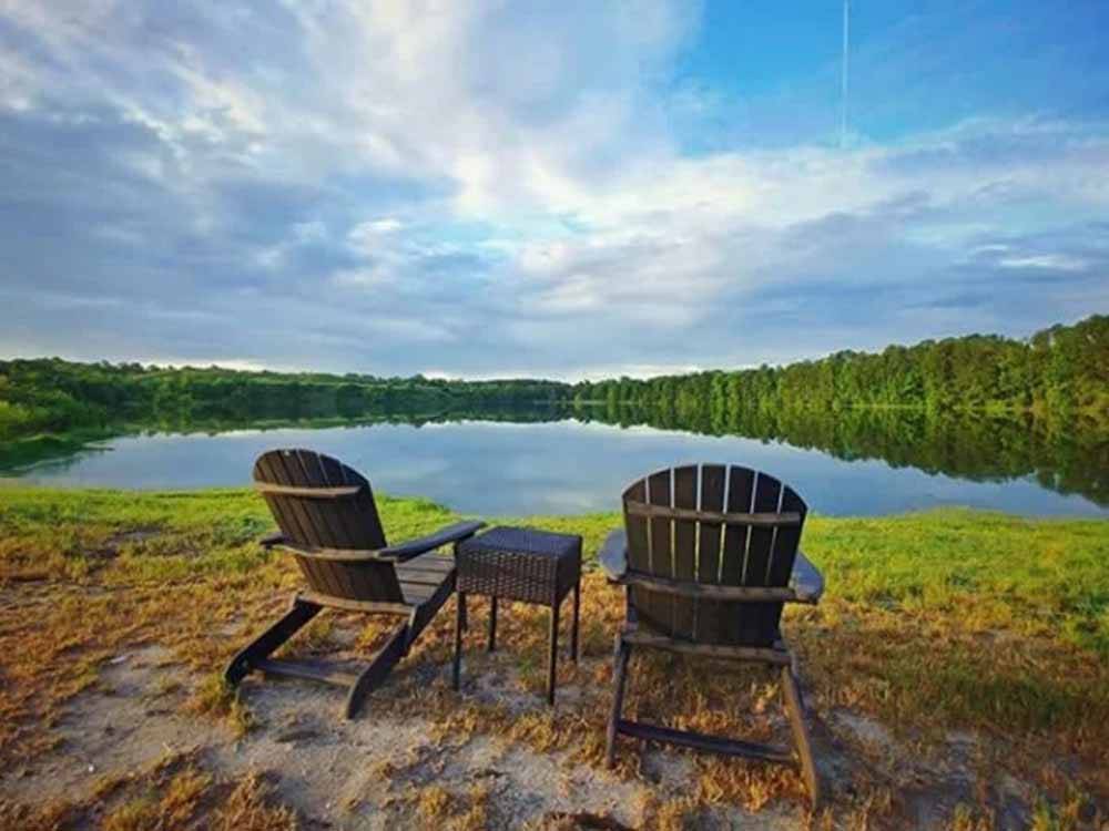 Two adirondack chairs and a table next to the lake at CREEKFIRE RESORT