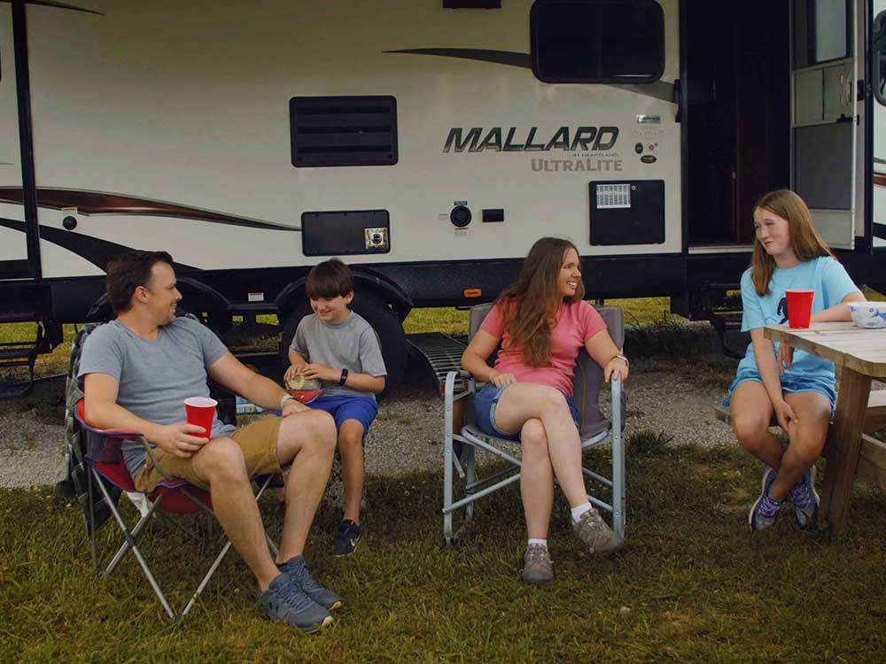 A family sitting outside of a motorhome at BIGFOOT ADVENTURE RV PARK & CAMPGROUND