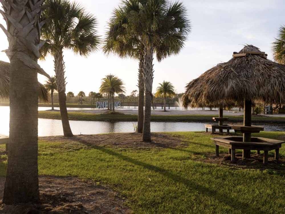 Benches with tiki huts next to the lake at RVs parked at dusk with water in distance at RESORT AT CANOPY OAKS