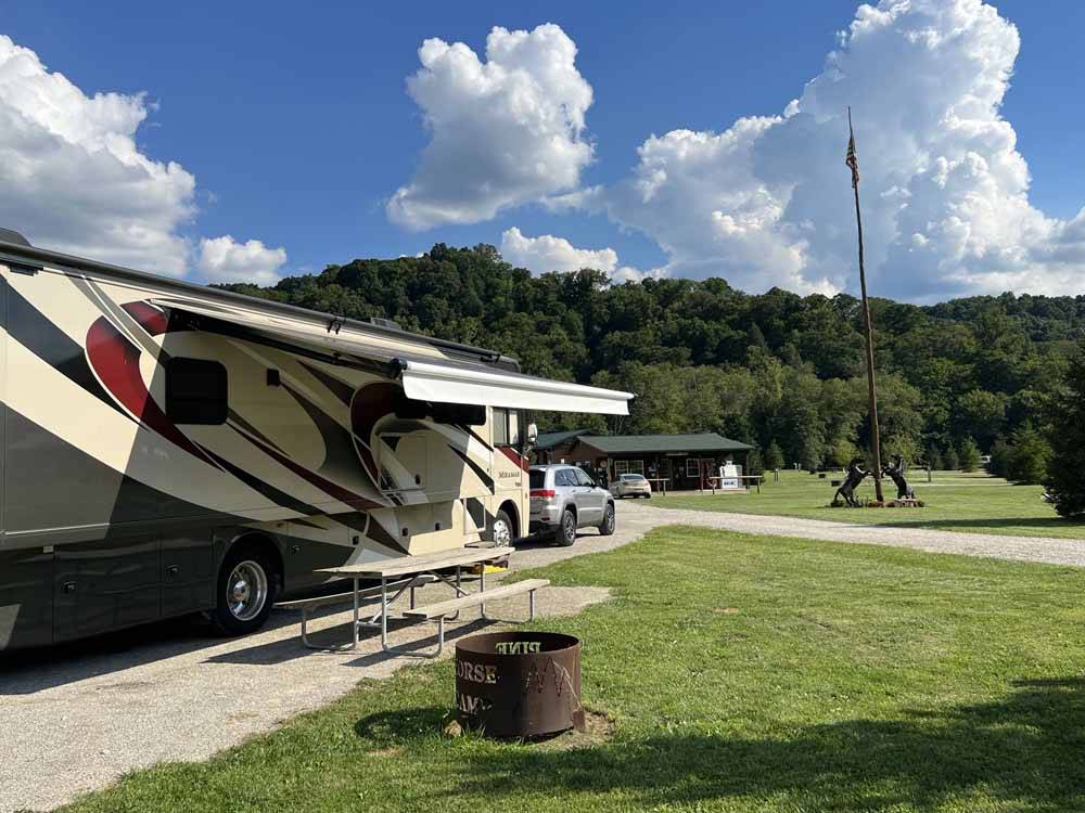 Motorhome with awning extended near picnic table and fire pit at PINE CREEK CABINS AND CAMPGROUND
