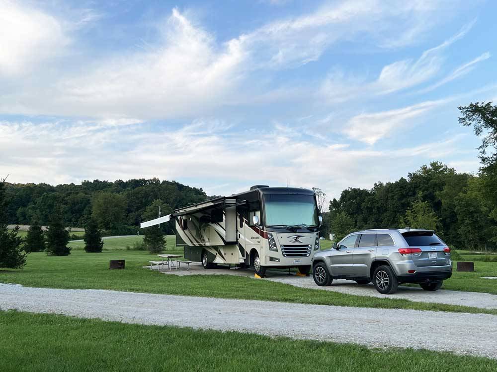 Gravel RV space with motorhome and SUV at PINE CREEK CABINS AND CAMPGROUND