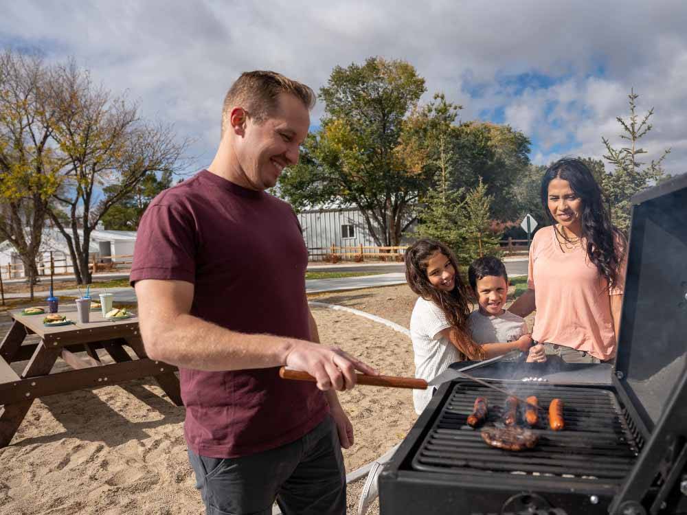 The dad barbecuing while the family looks on at LITTLE AMERICA RV PARK