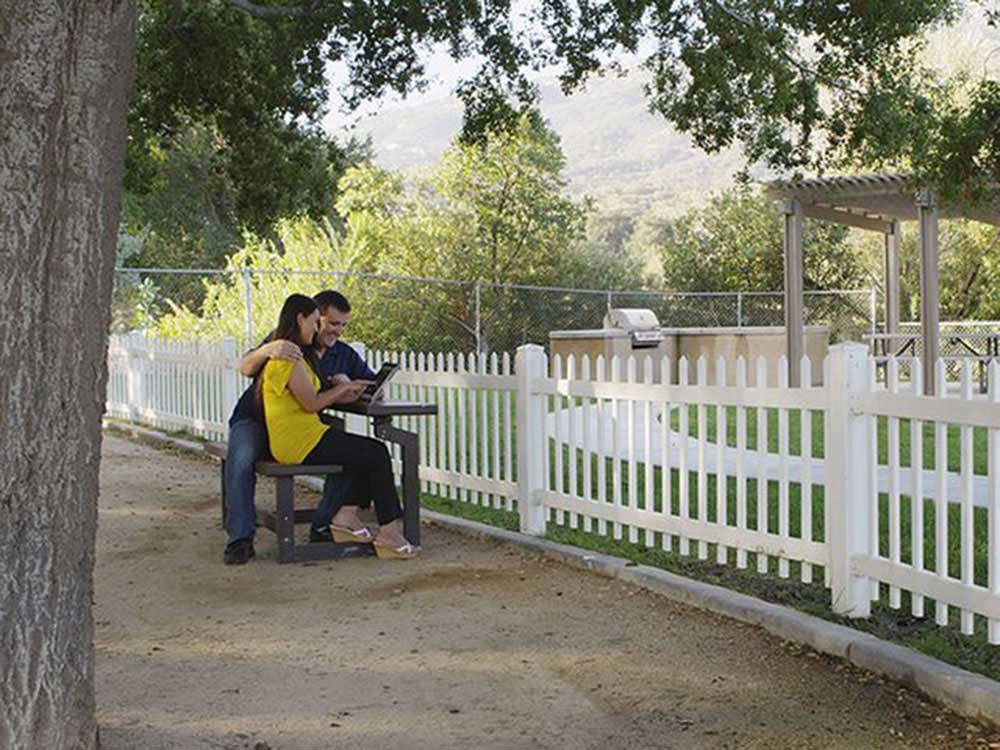 A couple sitting on a bench under a tree at PECHANGA RV RESORT