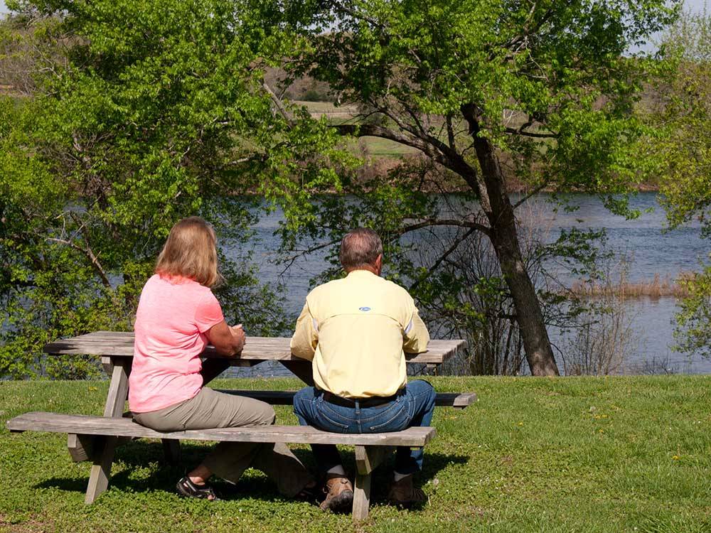 A man and woman on a picnic bench overlooking a river at DENTON FERRY RV PARK & CABIN RENTAL