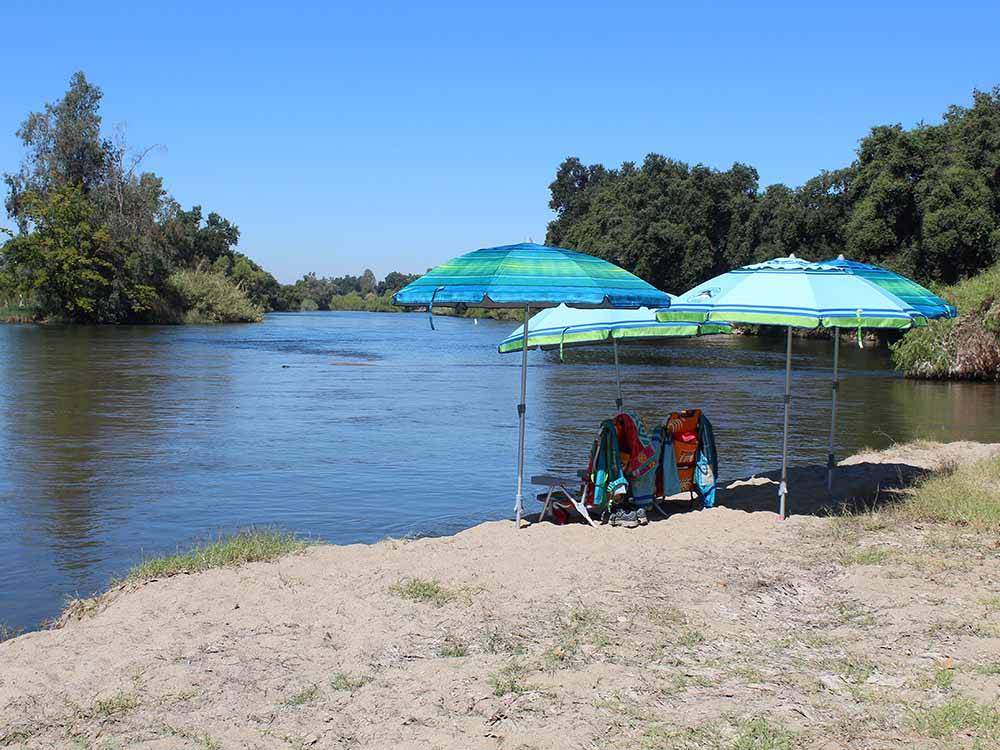 A couple of chairs under umbrellas by the river at KINGS RIVER RV RESORT