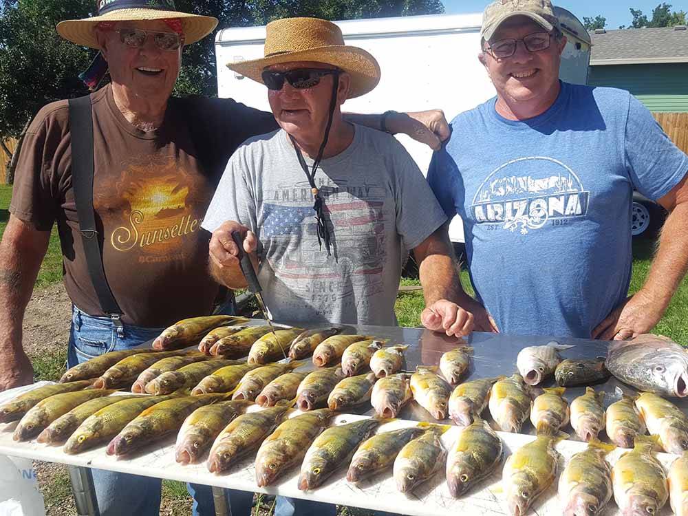 Three men standing with fish that they are getting ready to cut at COUNTY LINE RV PARK & CAMPGROUND