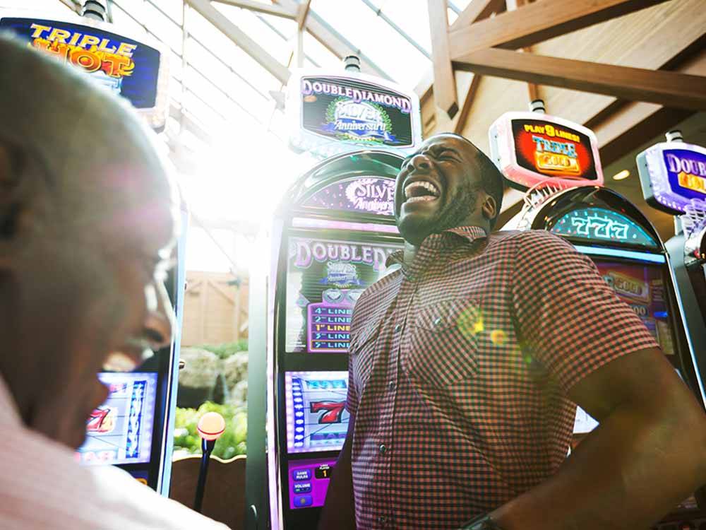 A couple of men laughing in front of slot machines at LITTLE RIVER CASINO RESORT RV PARK