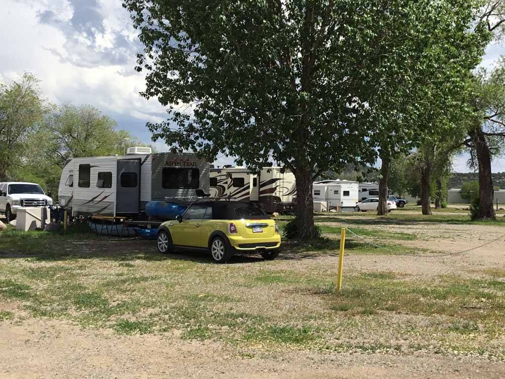 A small yellow car parked under a tree at SKY UTE FAIRGROUNDS & RV PARK