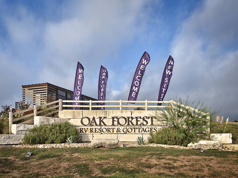 The front entrance sign with Welcome flying flags at OAK FOREST RV RESORT