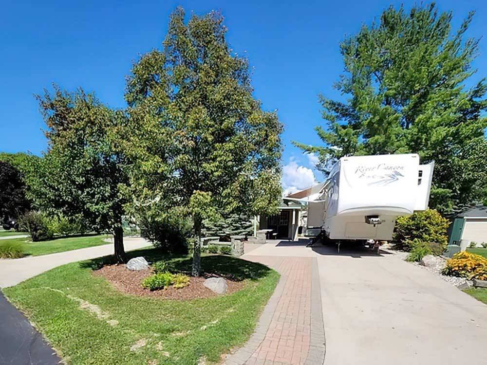 Fifth-wheel on paved site surrounded by trees at TRAVERSE BAY RV RESORT