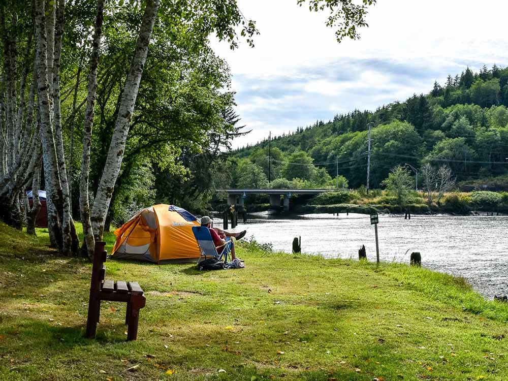 An man in a chair by a tent looking at the river at HOQUIAM RIVER RV PARK