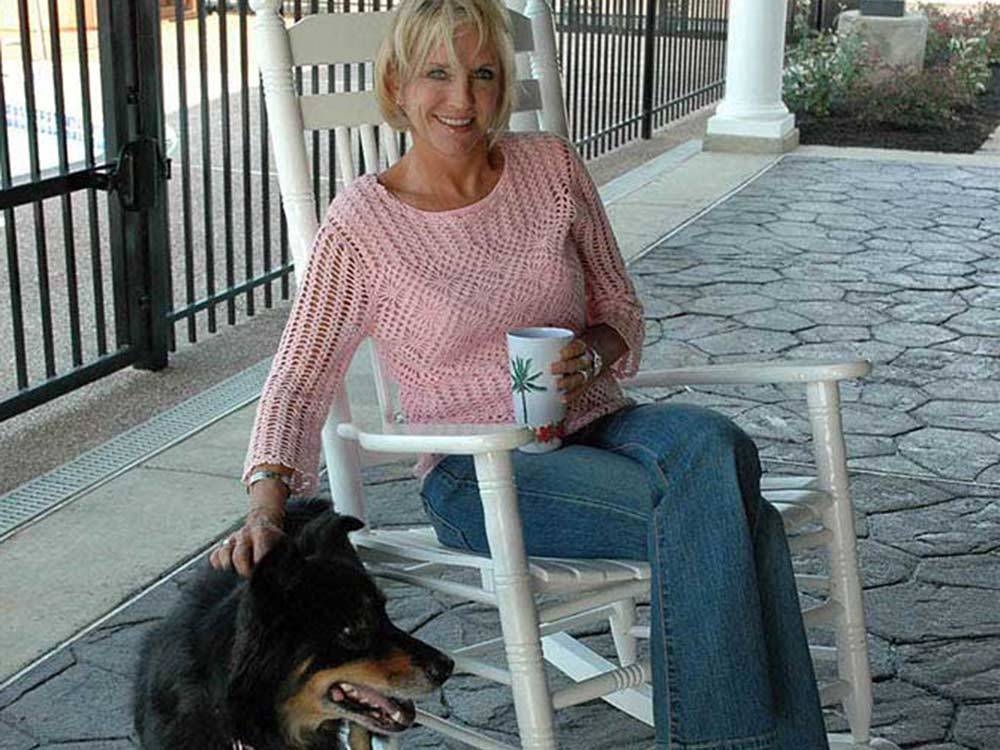Woman in white rocking chair petting black dog at EZ DAZE RV PARK
