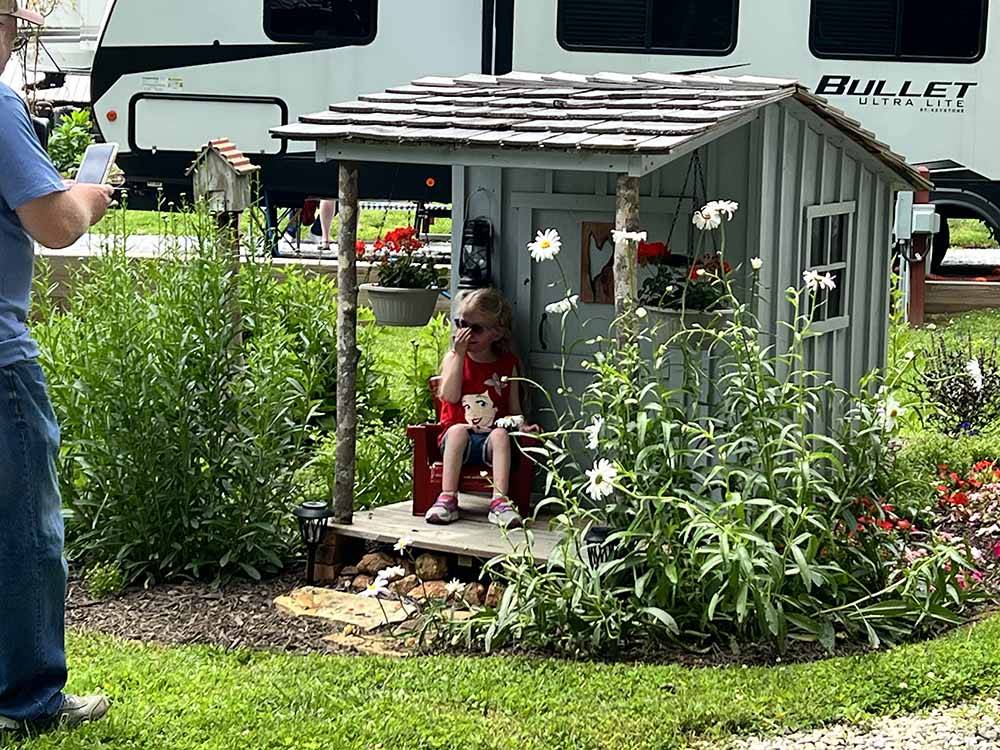 A little girl having her picture taken by a small house at A motorhome in a gravel RV site with a patio at FRANKLIN RV PARK & CAMPGROUND