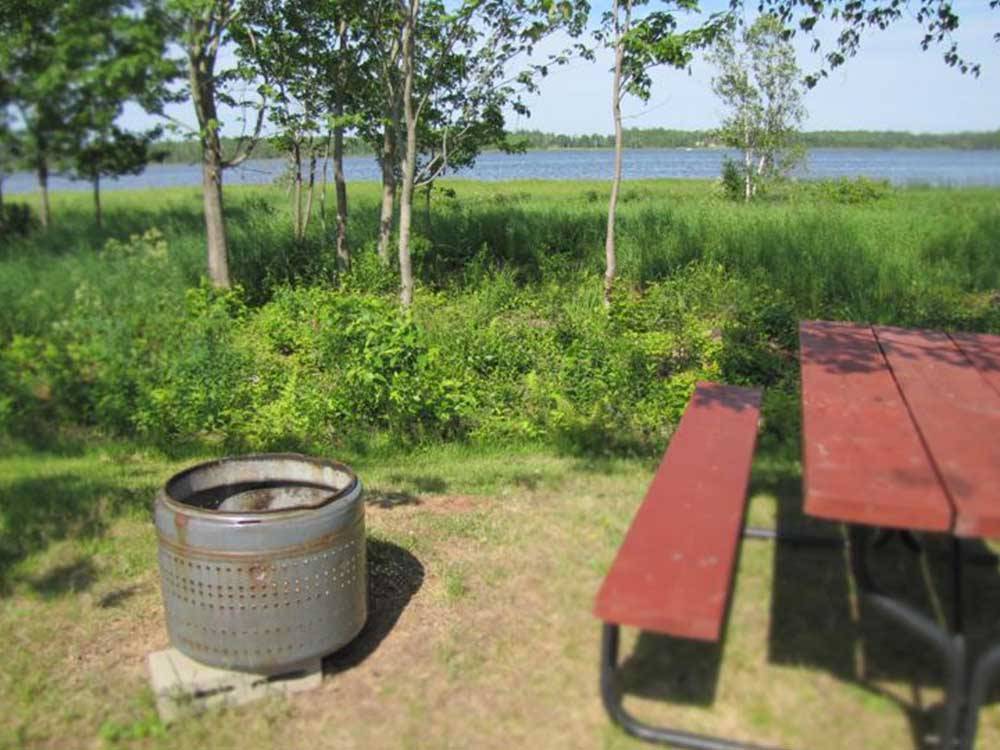 Picnic table and fire pit near water at CAMPING POKEMOUCHE