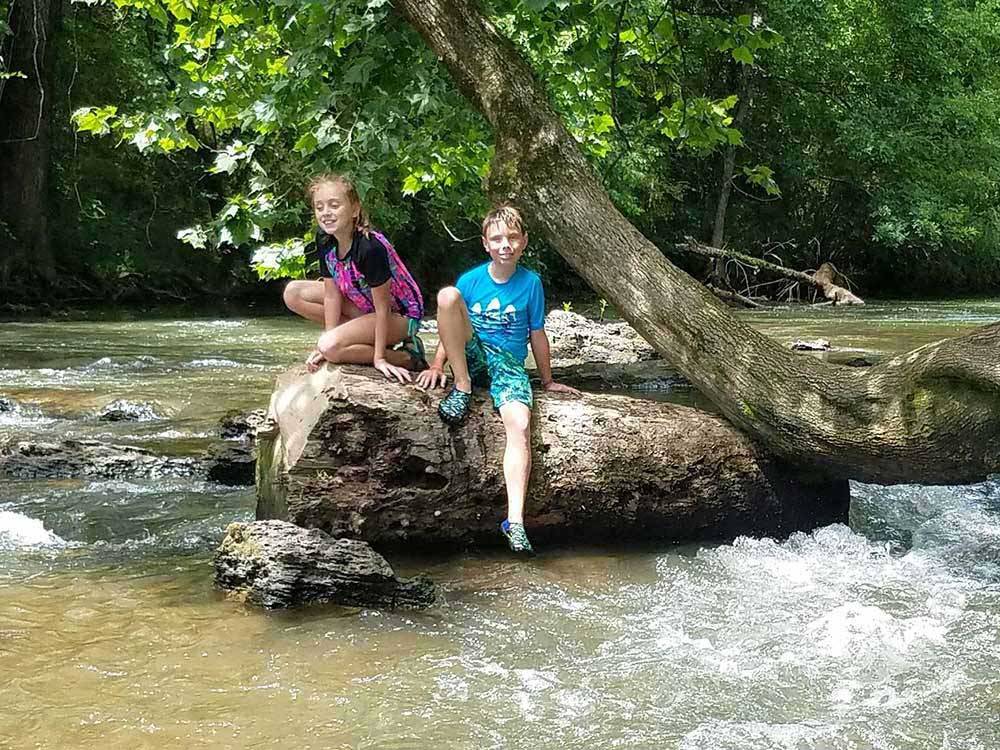 Kids sitting on a rock in the river at CEDAR CREEK RV & OUTDOOR CENTER