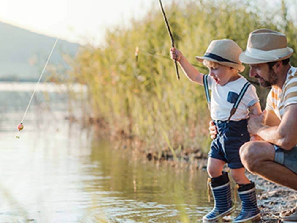 A man fishes with a little boy in a lake at MADISON VINES RV RESORT & COTTAGES