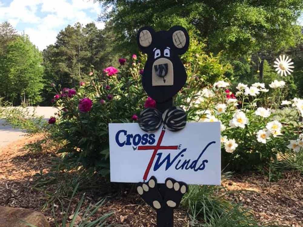 A small Cross Winds sign being held by a wooden bear at CROSS WINDS FAMILY CAMPGROUND
