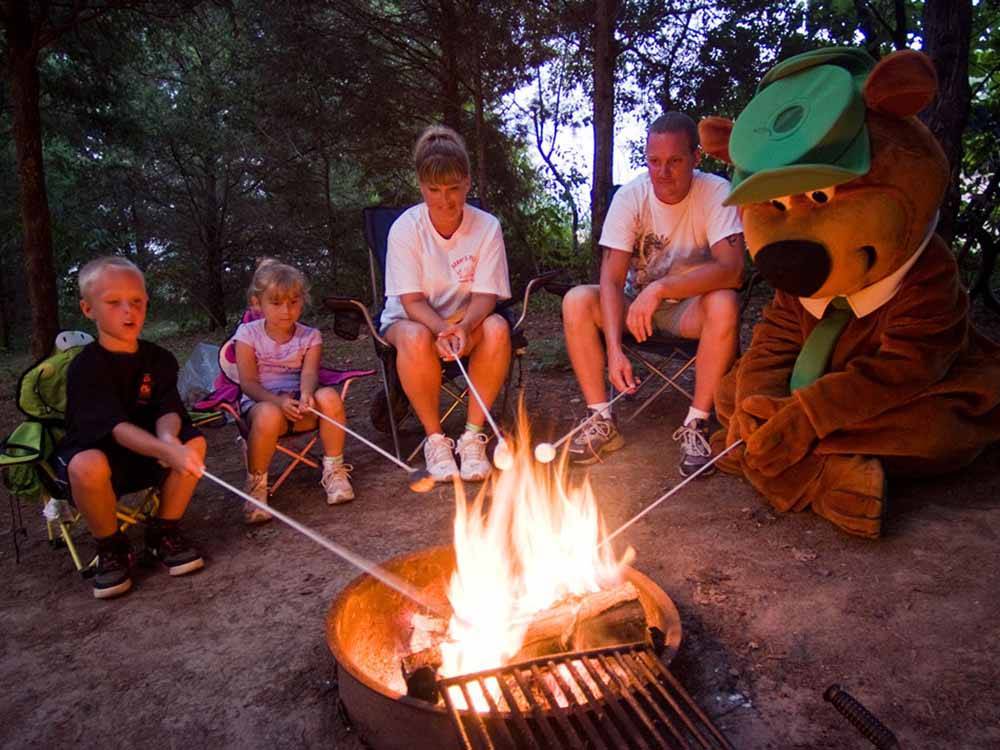 A family roasting marshmallows around a campfire with Yogi Bear at YOGI BEAR'S JELLYSTONE PARK AT DELAWARE BEACH
