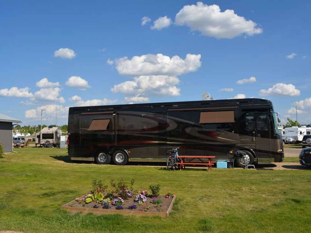 Class A RV camping near flower bed with picnic table  at ST. ALBERT RV PARK