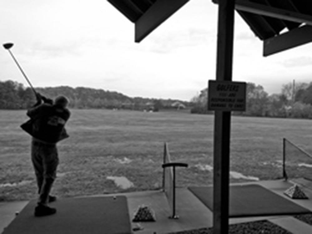Black and white photo of golfer swinging at the driving range at RIVERSIDE GOLF & RV PARK