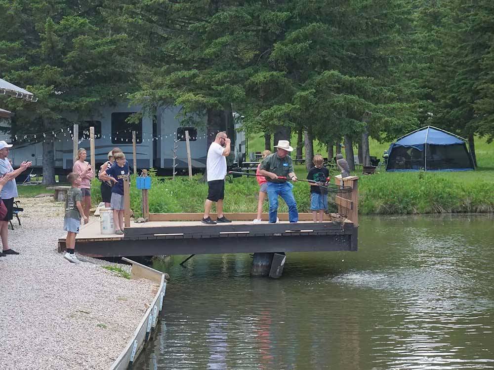 Man on fishing dock lifts up a fish with net at FISH'N FRY CAMPGROUND & RV PARK