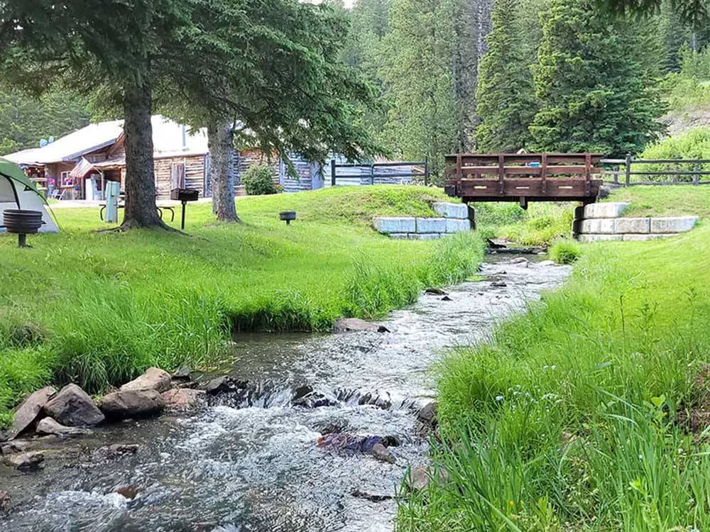 Stream rushes under a bridge and past grassy banks at FISH'N FRY CAMPGROUND & RV PARK