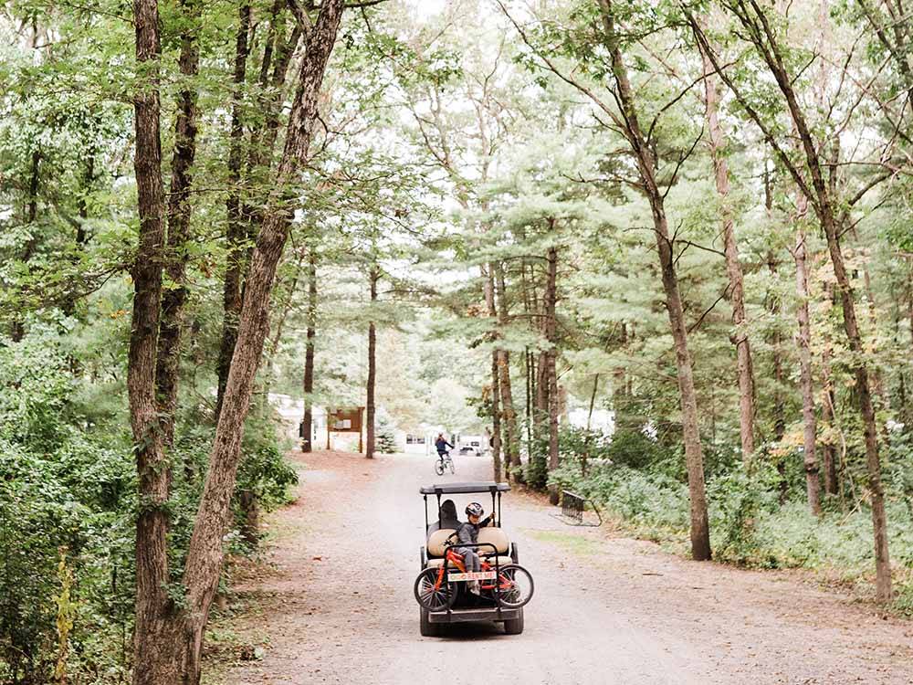 A couple driving a golf cart down a dirt path at NORMANDY FARMS FAMILY CAMPING RESORT