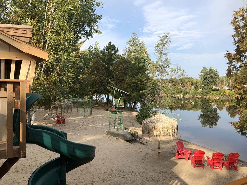 A sitting area and playground by the water at SID TURCOTTE PARK CAMPING AND COTTAGE RESORT