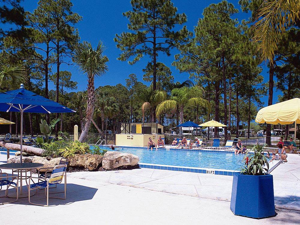 People lounging pool side, tables with umbrellas and decorative rock formation at ENCORE SUNSHINE HOLIDAY DAYTONA