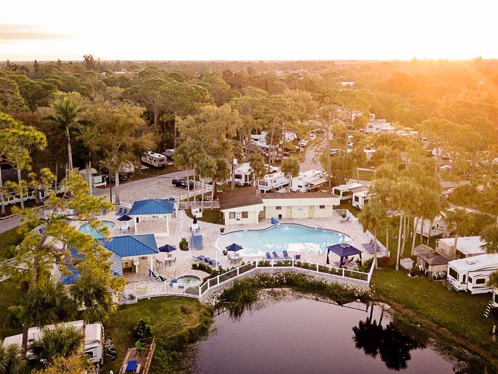 Aerial view of a resort with pond, pool and RVs amid tall trees at BLUEWAY RV VILLAGE