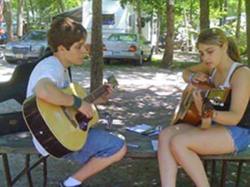 Two people hanging out playing acoustic guitars at ATLANTIC SHORE PINES CAMPGROUND