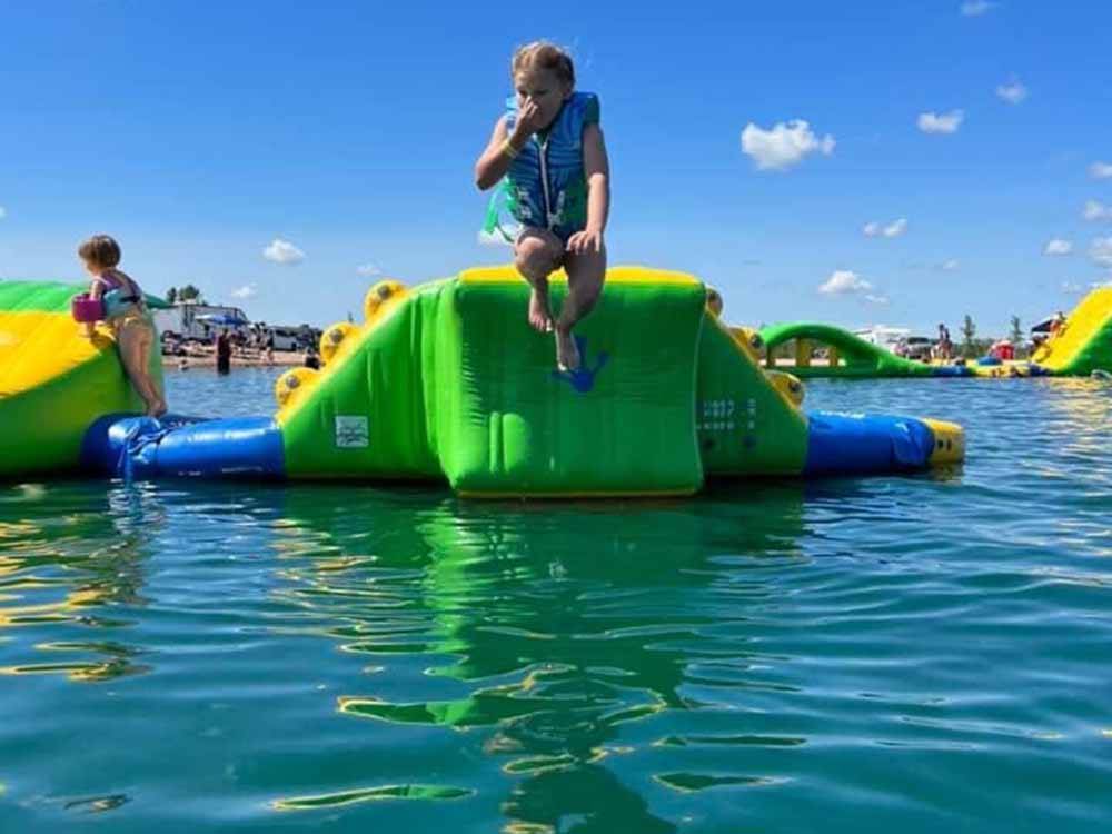 A kid jumping off an inflatable slide on the lake at STONEY CREEK RV RESORT