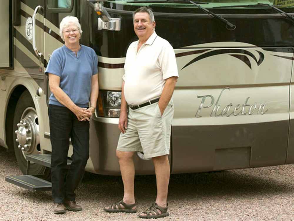 A couple standing in front of a motorhome at GOLDFIELD RV PARK
