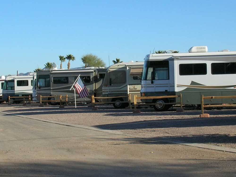 Row of RVs in sites separated by wooden fences at 88 SHADES RV PARK