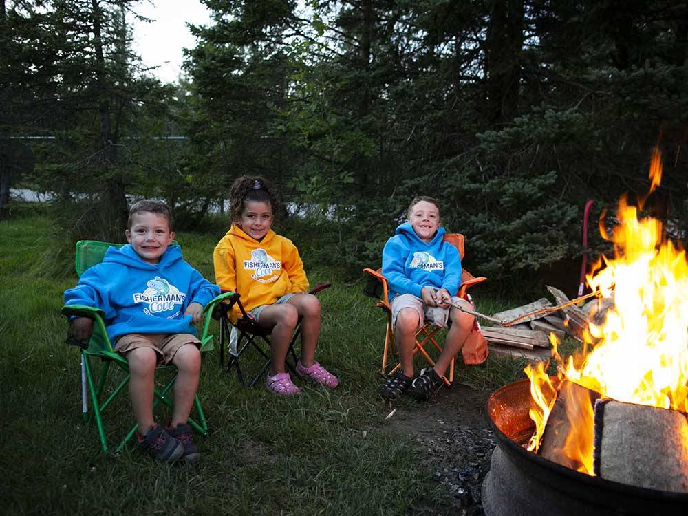 Three young kids sitting by a fire pit at FISHERMAN'S COVE TENT & TRAILER PARK