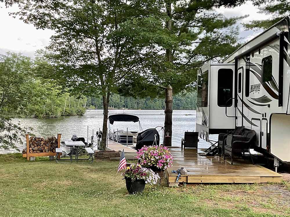 An RV site with a wooden patio by the water at AUGUSTA-WEST LAKESIDE KAMPGROUND