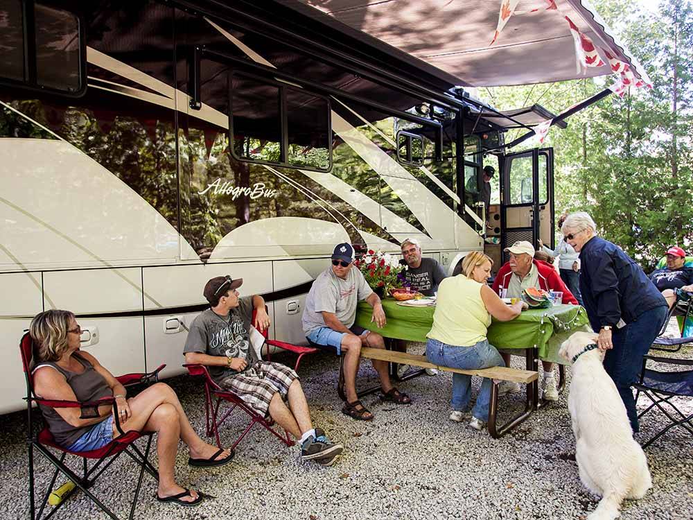 A group of people eating along side of a motorhome at SUMMER HOUSE PARK