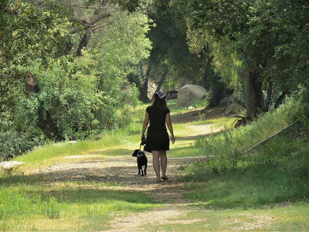 Woman walking a dog on wooded trail at RANCHO LOS COCHES RV PARK